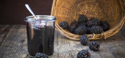 Basket of blackberries (Rubus sectio Rubus) and preserving jar of blackberriy jelly on wooden table