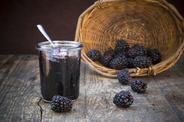 Basket of blackberries (Rubus sectio Rubus) and preserving jar of blackberriy jelly on wooden table